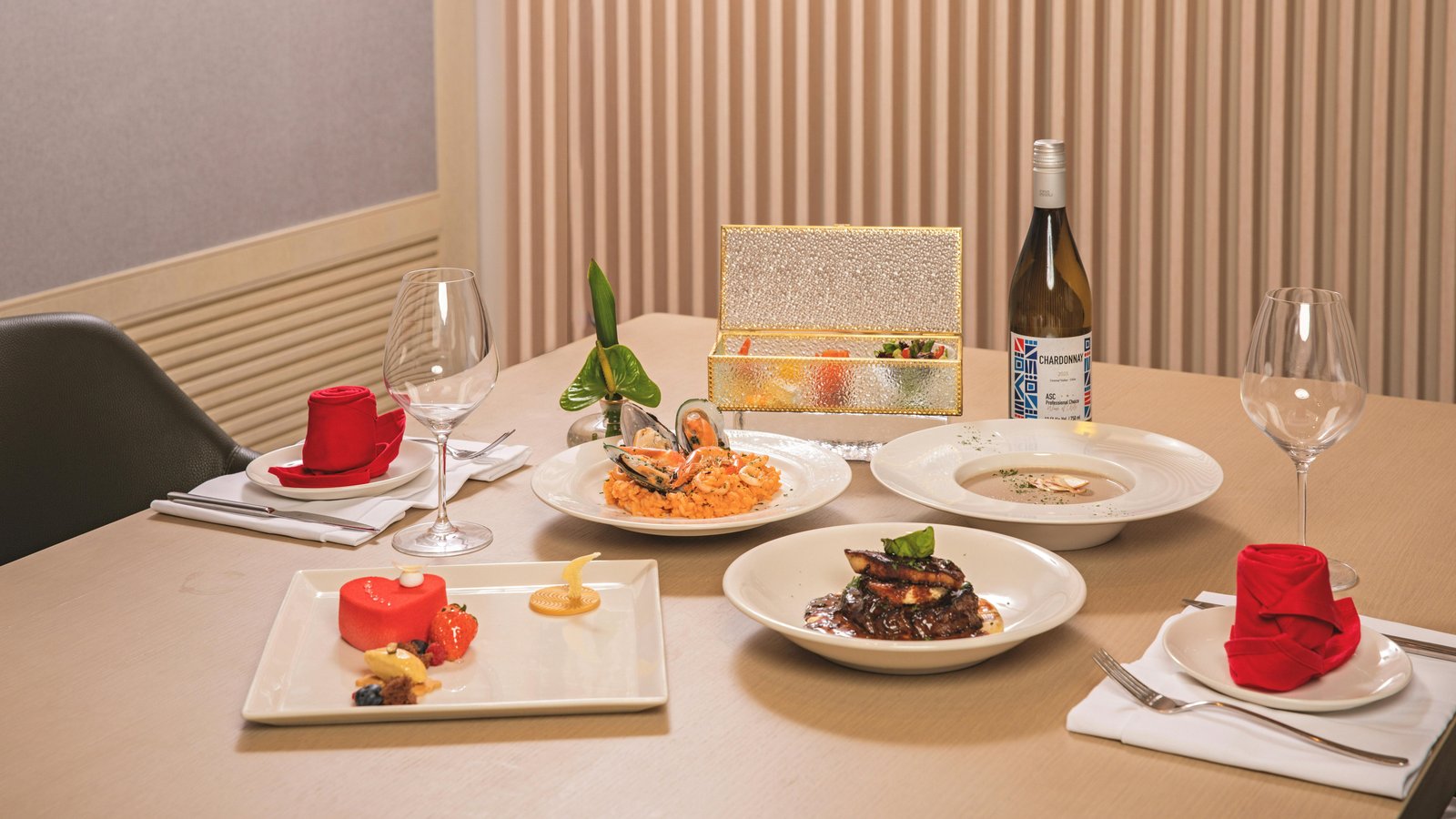 Chef arranging gourmet plated course on elegant table with wine glasses and fresh flowers.