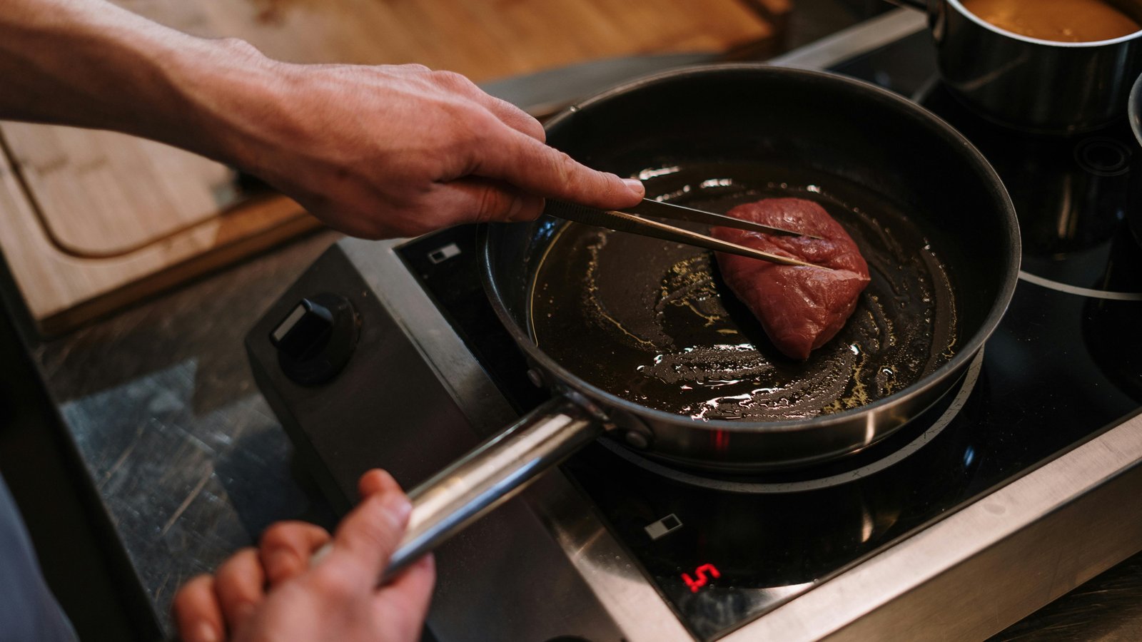 Chef searing Colorado elk steak in a luxury Aspen kitchen with mountain views through windows.